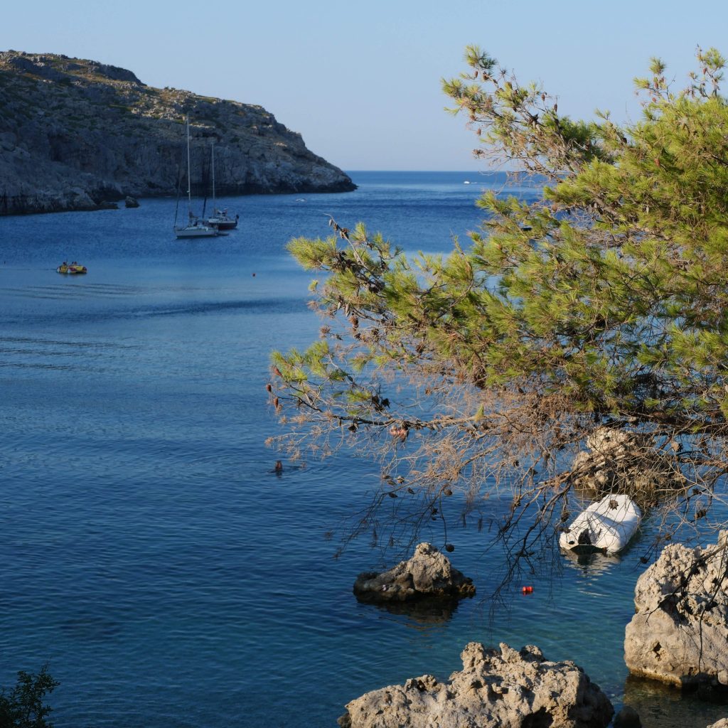 Crique de Rhodes avec voiliers ancrés entre pins et eau turquoise, une île parfaite pour un voyage en Grèce en famille.